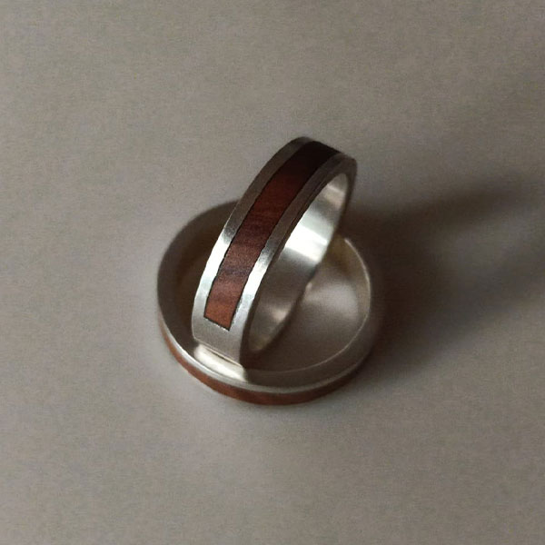 Dos anillos Línea Olivo Plata reposan en una superficie neutra, mostrando su acabado en plata reciclada y elegantes incrustaciones de madera de olivo.