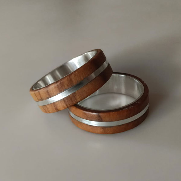 Dos anillos artesanales de madera de olivo y plata reciclada, uno sobre el otro, destacan sobre una superficie clara.