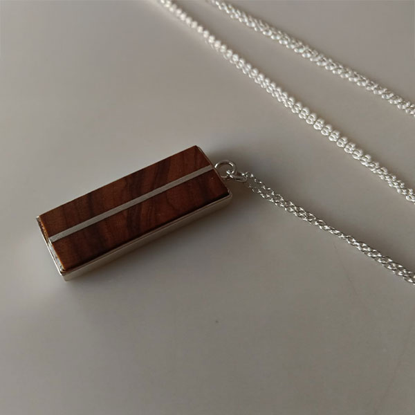 Colgante rectangular de madera de olivo y plata reciclada, con una franja plateada y cadena de plata, sobre fondo claro.