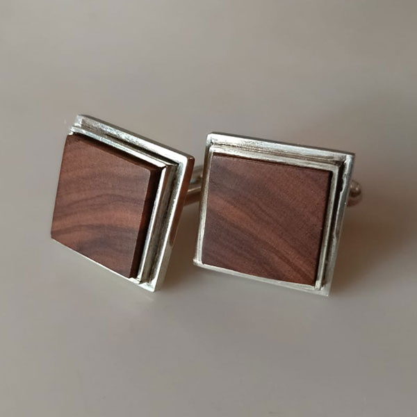 Gemelos cuadrados en plata reciclada con una fina incrustación de madera de olivo, elegantes y artesanales, sobre fondo neutro.